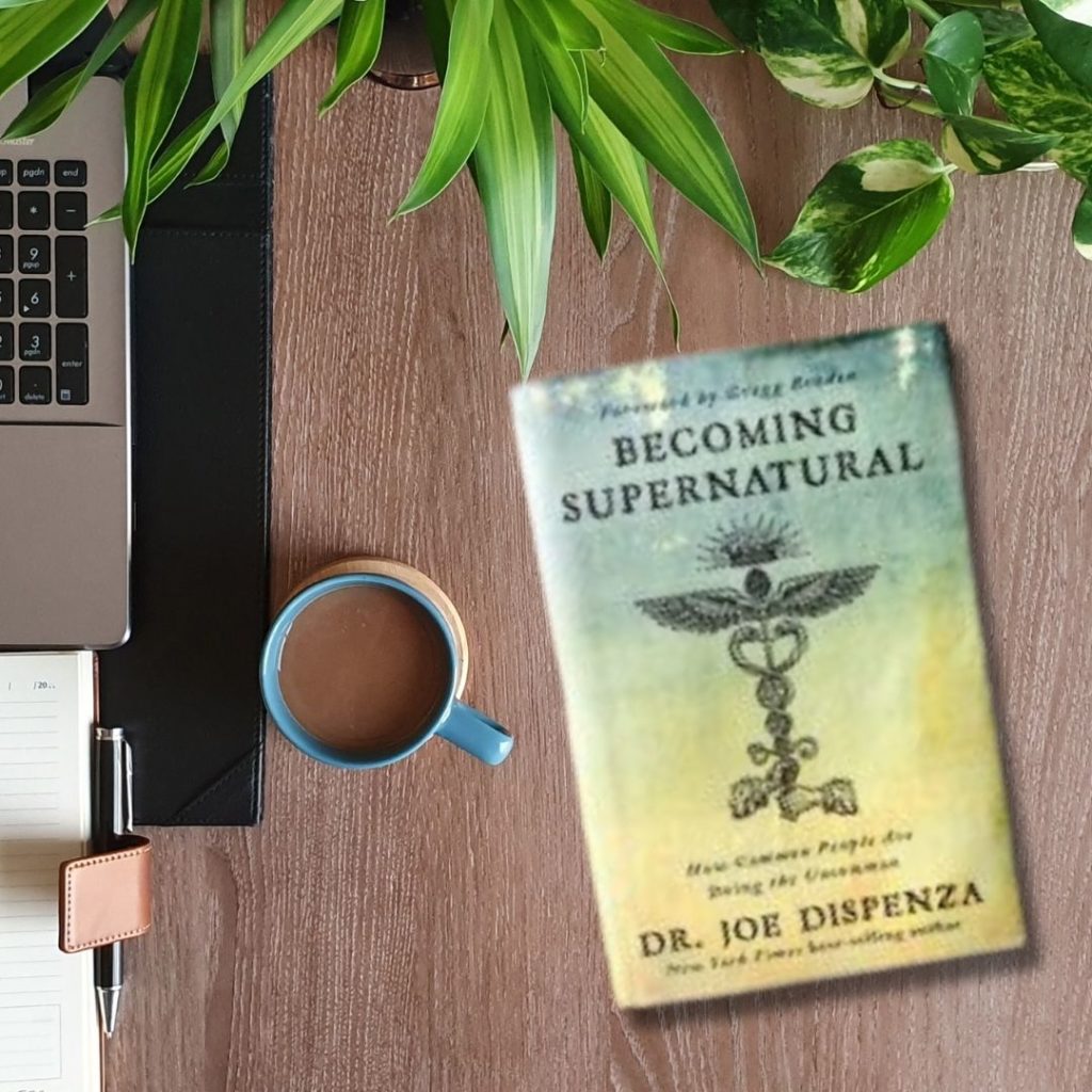 being supernatural by dr. joe dispenza on desk next to laptop and chai